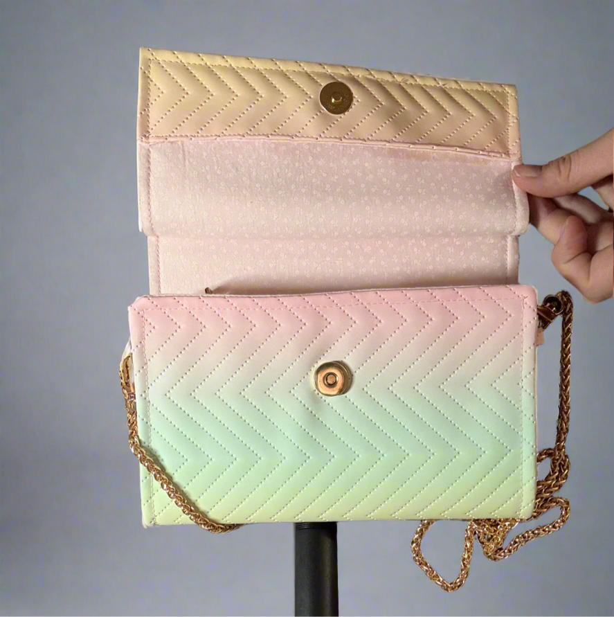 A close-up of an open, handcrafted clutch purse. The purse has a flap closure and a delicate gold chain strap. The material is quilted in a chevron design, and the colors transition smoothly from a light green at the bottom, through a pale yellow in the middle, to a very light pink on the top flap. The flap is open, revealing the inside of the purse which has a zippered compartment. The magnetic snap is gold.