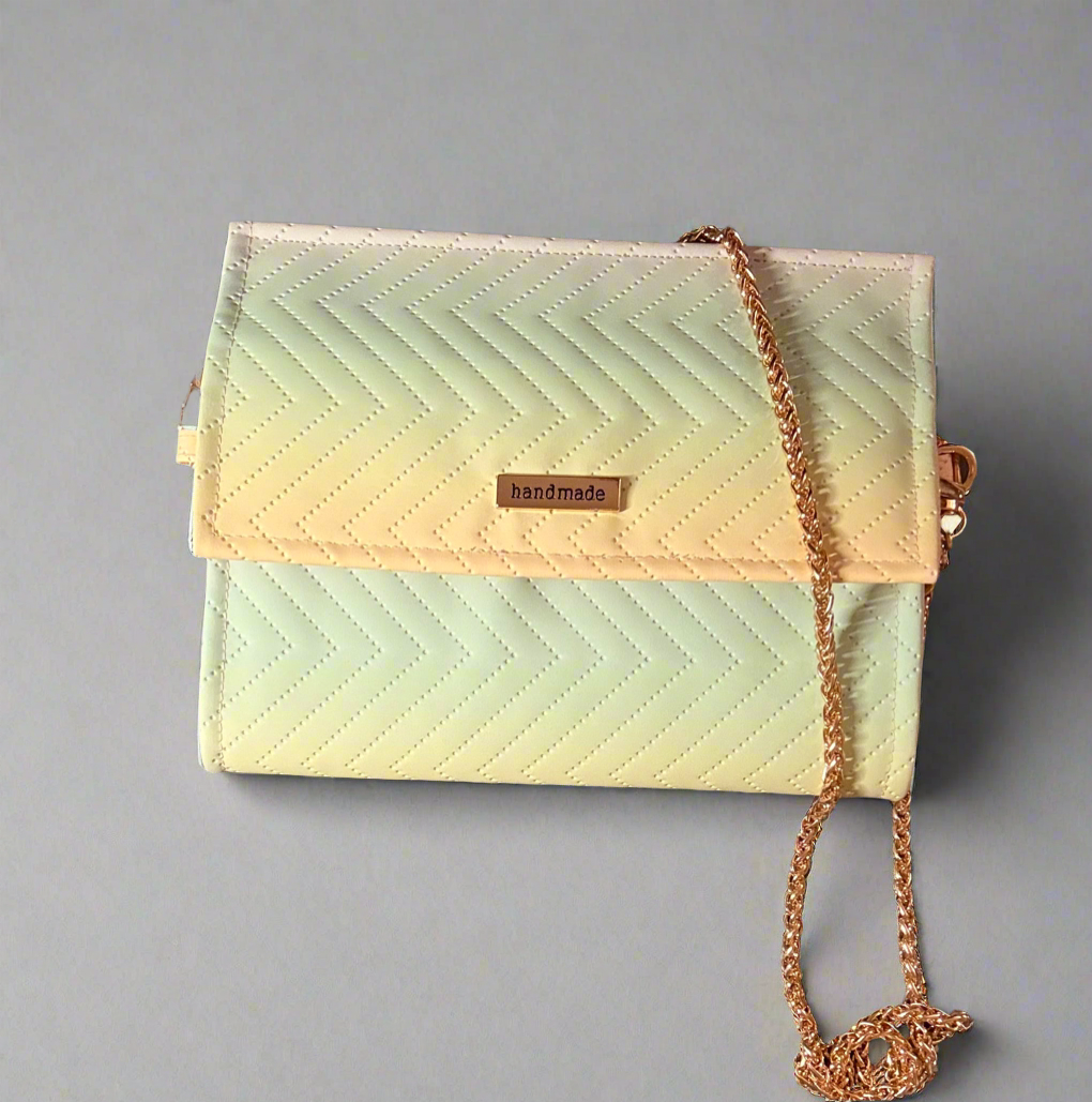 A small, rectangular clutch purse featuring a handmade quilted chevron pattern in a soft pastel gradient of green, yellow, and pink. The purse has a gold chain shoulder strap and a gold-toned "handmade" tag on the front flap.