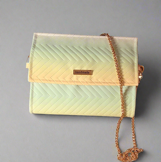 A small, rectangular clutch purse featuring a handmade quilted chevron pattern in a soft pastel gradient of green, yellow, and pink. The purse has a gold chain shoulder strap and a gold-toned "handmade" tag on the front flap.