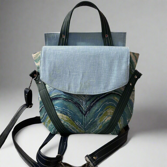 Picture of convertible handbag/backpack. It has a light blue flap, dark blue handles, strap, and accents, and a blue wave patterned front.